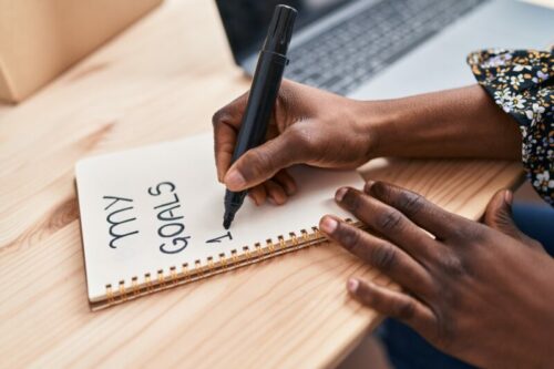 African american woman ecommerce business worker using laptop writing on notebook at office